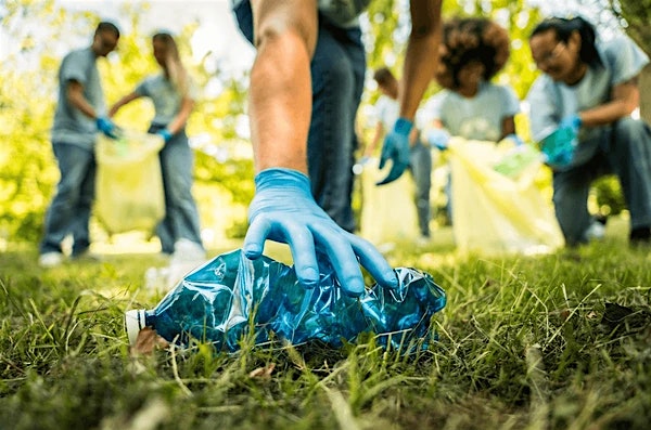 Volunteer wearing blue gloves picks up a crumpled plastic bag in a park during a cleanup session.