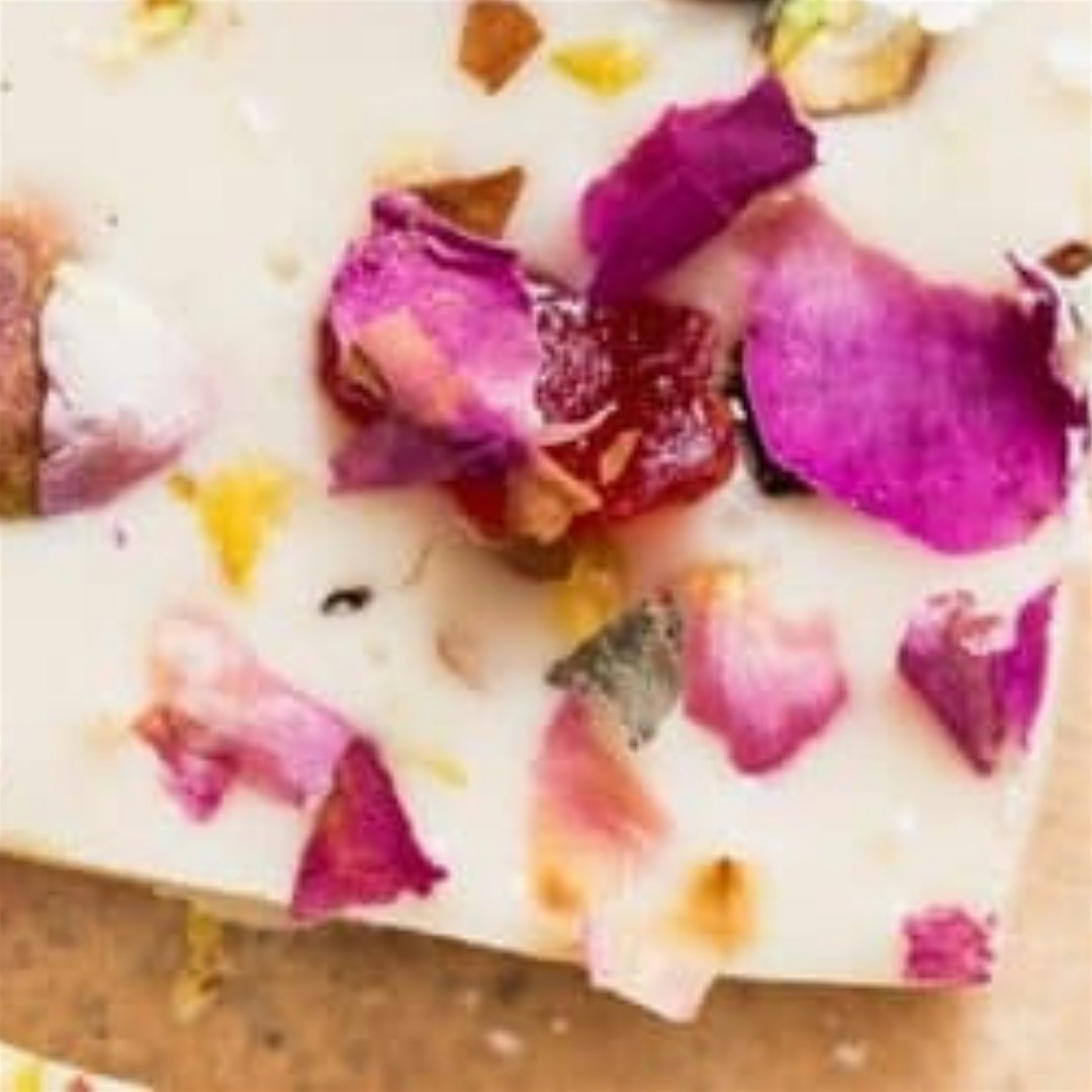 Close-up of a dessert garnished with pink and purple edible flower petals on a white plate.