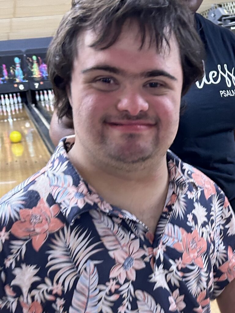 IMG_2454 - PARENTGUIDENEWS Close-up of a smiling man with dark hair wearing a pink and blue floral shirt, at a bowling alley.