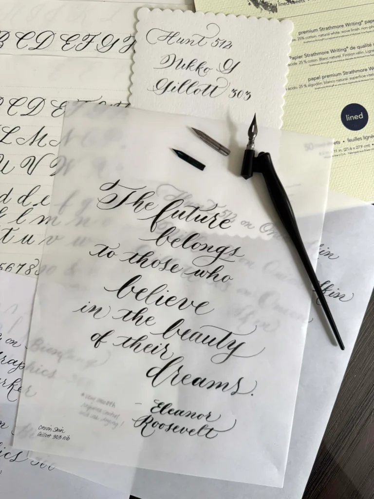 Modern_Calligraphy_-1-4ZX7PT - PARENTGUIDENEWS Close-up of a dip pen and nibs resting on layered calligraphy practice sheets with elegant cursive writing.